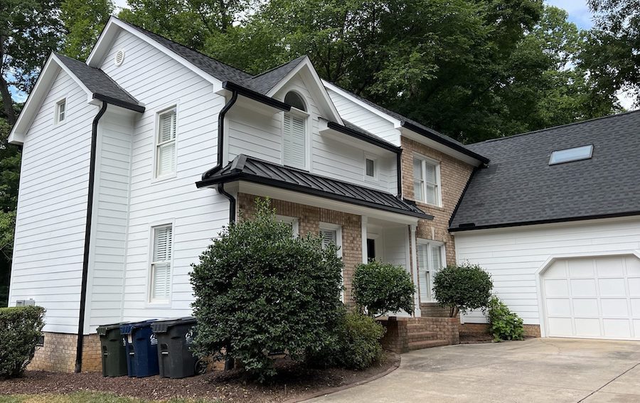 Home in Huntersville, NC with white siding black roofing and brick work after quality home exterior remodeling.