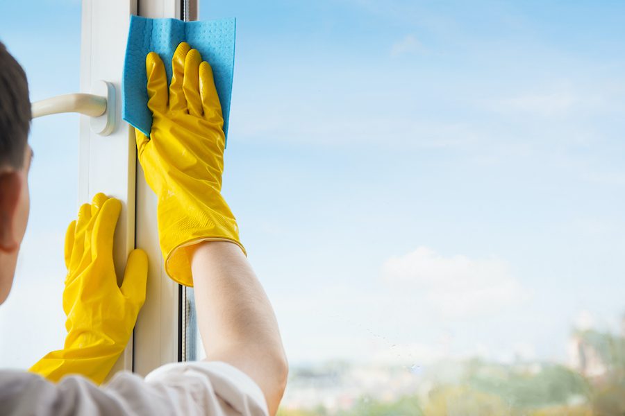 Man in yellow gloves cleaning window with rag and spray detergent at home terrace.